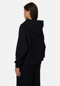 Zwarte oversized hoodie van zachte stof, met een trekkoordcapuchon, geribbelde manchetten en een ontspannen pasvorm, zonder zichtbare logo's of patronen.