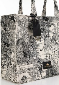 Sac en toile noir et blanc avec un motif tropical featuring des tigres et des palmiers. Inclut une étiquette en cuir noir avec le logo.