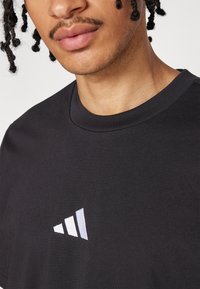 Zwarte katoenen t-shirt met een ronde halslijn, voorzien van een klein, wit logo met drie lijnen in de linkerbovenhoek.