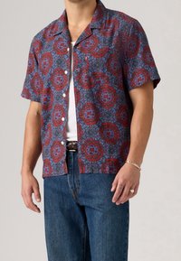 Koszula z krótkim rękawem w kolorze czerwonym i niebieskim z kwiatowym wzorem, z zapięciem na guziki z przodu i kieszonką na piersi, wykonana z lekkiego materiału.