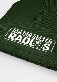 Green knit beanie with a textured pattern and a rectangular white patch featuring the text "ICH BIN SELTEN RADLOS" and a bicycle icon.