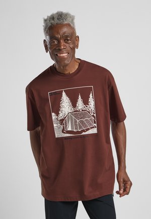 Bordeaux katoenen t-shirt met een witte grafiek van een tent en bomen, met de tekst "Making room to roam" onder de illustratie. Korte mouwen.