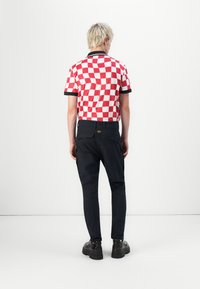 Short-sleeve polo shirt with a red and white checkered pattern, black collar, paired with dark pants and black shoes. Rear view.