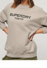 Felpa grigia chiara con scollatura a girocollo a coste, vestibilità oversize e "SUPERDRY TOKYO" stampato in bold nero sulla parte anteriore.