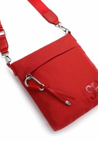 Pequeño bolso cruzado rojo con textura, correa ajustable, bolsillo frontal con cremallera y cierres metálicos plateados sobre un fondo blanco.