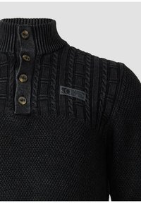 Czarny sweter dziany z prążkowanym wysokim kołnierzem, czterema guzikami na zapięciu z przodu, detalami w splot warkoczowy oraz małą łatką z logo na piersi.