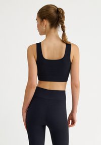 Top corto negro de canalé con escote cuadrado, combinado con leggins de cintura alta, que muestran un material texturizado y un diseño ajustado.