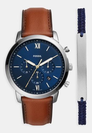 Brunt läderrem klocka med en blå urtavla, silverdetaljer, tre subskivor och datumsdisplay. Inkluderar ett marinblått flätat armband.