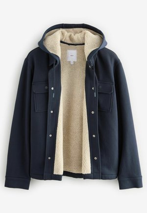 Giacca blu navy con un morbido rivestimento in pile crema, chiusure frontali a pressione, due tasche sul petto e un cappuccio. Esterno texturizzato con un design accogliente.