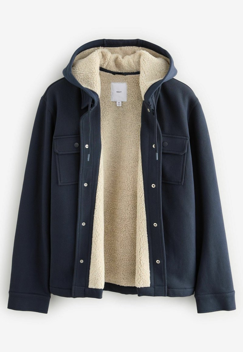 Navy blue jacket with a soft cream fleece lining, front snap closures, two chest pockets, and a hood. Textured exterior with a cozy design.