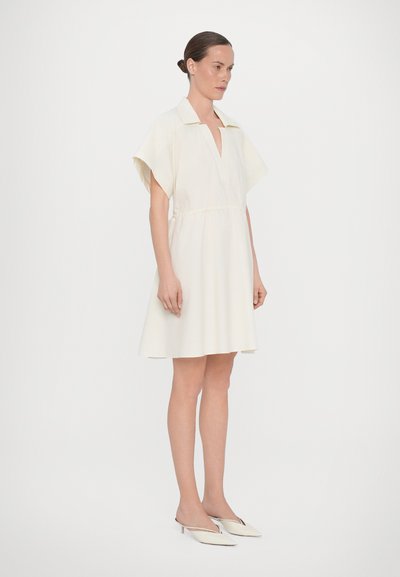 Vit klänning med spetsig krage, korta ärmar och elastisk midja. Slät textur och avslappnad passform, parat med off-white mule-skor.