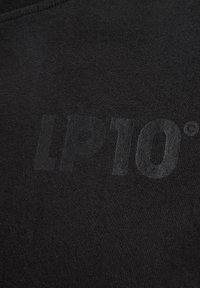 Sort stof med en glat tekstur, der har et subtilt, blankt 'LP10°' logo i midten, som blander sig en smule med materialet.
