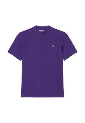 Camiseta de algodón morada con mangas cortas, escote redondo y un pequeño logo de cocodrilo verde en el lado izquierdo del pecho. Textura suave.
