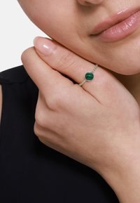 Anello d'argento con pietra di malachite a strisce verdi, con una delicata fascia di perline. La mano si appoggia delicatamente sulla guancia.