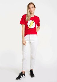 Red cotton t-shirt featuring a large yellow lightning bolt on a white circle. Paired with white pants and black athletic shoes.