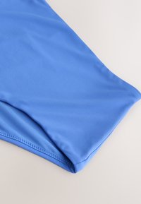 Sinine kangas, mille serv on lõigatud ja õmmeldud, lebamas lamedalt heledal pinnal, näidates sujuvat tekstuuri ja korralikke õmbluse detaile.