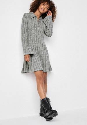 Robe grise en tricot avec un col, texture côtelée et manches longues, associée à des bottines noires à bout arrondi avec des accents de boucle.