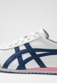 Vit sneakers med blå och rosa detaljer. Har en texturerad läderöverdel, kontrasterande ränder och en gummisula.