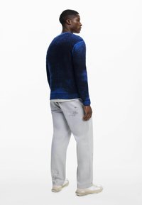 Suéter azul con degradado y textura acanalada, combinado con pantalones gris claro con acentos estampados y zapatillas beige.