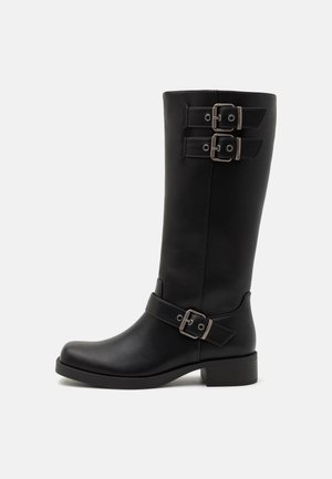 Bottes noires montantes en cuir lisse, dotées de deux boucles en métal argenté et d'un talon carré. Le design est élégant et moderne.