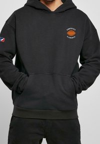 Felpa nera con cappuccio e tasca frontale, caratterizzata da una grafica di un pallone da football e il testo "Football Gameday". Materiale morbido e polsini e orli a coste.