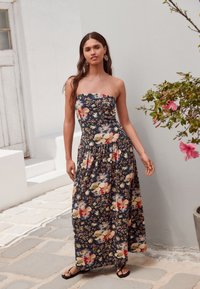 Sukienka maxi bez ramiączek w granatowym materiale z kwiatowym wzorem w kolorach beżowym, czerwonym i zielonym. Luźny fason z elastycznym paskiem w talii.