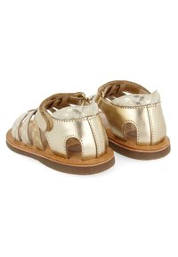 Gouden sandalen met zachte leren banden, open teen- en hielontwerp, met een geometrisch patroon op de banden en een bruine rubberen zool.
