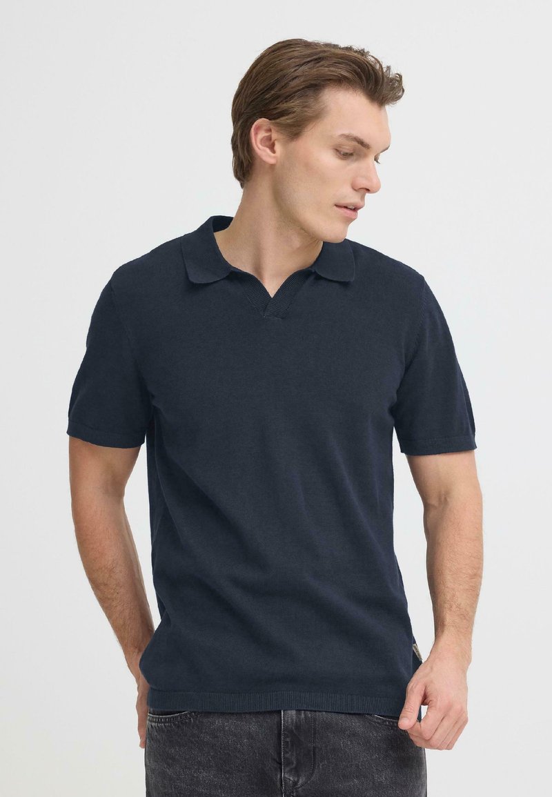 Polo bleu marine à manches courtes en maille douce, avec un col à encolure en V et des poignets côtelés aux manches.