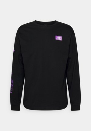 Camiseta negra de manga larga con cuello redondo, con pequeño logo de New Balance en color púrpura en el pecho izquierdo y gráficos de texto púrpura en la manga derecha.