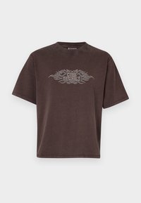Brūns pārāk liels T-krekls, kas izgatavots no kokvilnas, ar īsām piedurknēm. Priekšpusē ir sudraba "Guess Originals" grafika ar liesmu akcentiem.