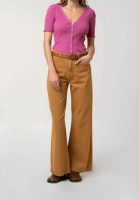 Růžový pruhovaný top s výstřihem do V a krátkými rukávy, zapínání na knoflíky, spárovaný s vysokými, širokými béžovými kalhotami a hnědými botami.