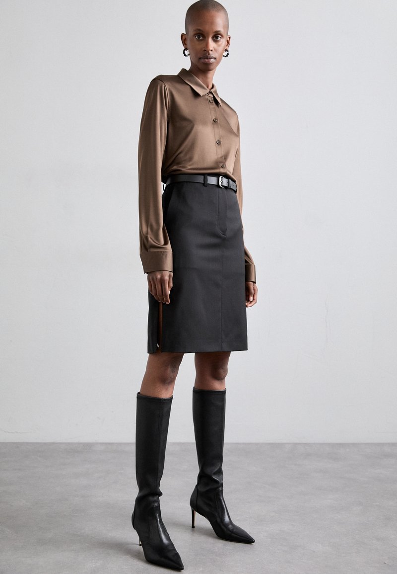 Brown long-sleeve button-up shirt with a collar, paired with a black knee-length skirt and sleek black knee-high heeled boots.