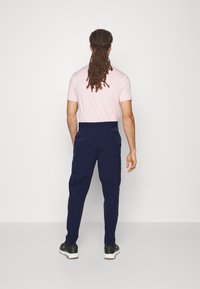 Mörkblå byxor med en slät textur och skräddarsydd passform, kombinerat med en ljusrosa t-shirt med kort ärm och avslappnade svarta sneakers.