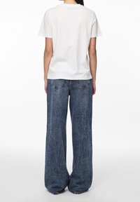 Bílý bavlněný tričko s krátkým rukávem, spárované s volnými, širokými modrými džíny z denimu s vybledlým vzhledem a zadními kapsami.