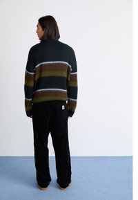 Multifarvet sweater med striber i grøn, brun og blå, lavet af et fuzzy materiale. Kombineret med sorte kordfløjspants og brune støvler.