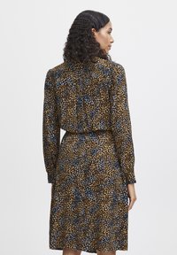 Langärmliges Kleid mit einem abstrakten Muster in Braun, Blau und Gold, cinchter Taille und fließender Silhouette. Glatte Stofftextur.