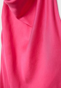 Kirkkaan vaaleanpunainen kangas, jossa on pehmeitä laskoksia ja sileä pinta, roikkuu vaaleaa taustaa vasten.