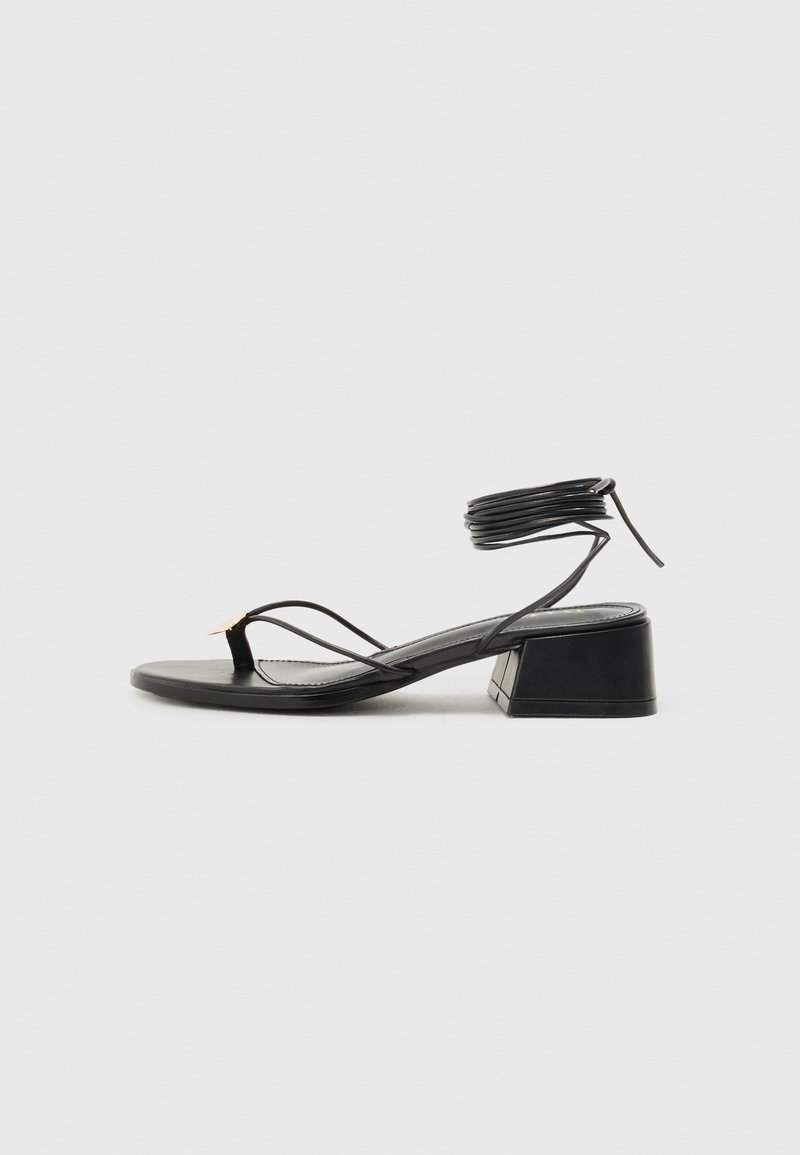 Sandalias negras de tacón con un tacón bloque triangular, tiras finas y un envoltura de tobillo. Textura suave con un diseño minimalista y un acento sutil.