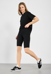 T-shirt noir à manches courtes associé à un short de vélo côtelé noir. La tenue est complétée par des baskets noir et blanc.