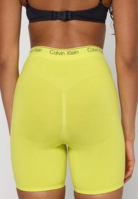 Żółte, jasne, wyszczuplające spodenki z wysokim stanem, dopasowane do sylwetki, z elastycznym paskiem w talii ozdobionym logo "Calvin Klein". Matowa faktura i gładkie wykończenie.
