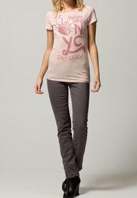 Světle růžové tričko s potiskem NYC a grafickým designem, kombinované s tmavě šedými slim-fit kalhotami a černými lodičkami. Hladký bavlněný materiál.