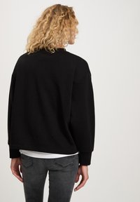 Czarna, oversize bluza z okrągłym dekoltem i opadającymi ramionami, zestawiona z szarymi dżinsami; charakteryzuje się gładką fakturą i luźnym krojem.