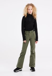 Top a maniche lunghe nero e pantaloni da neve verde oliva con due tasche frontali e una cintura regolabile nera. Stivali neri completano l'outfit.