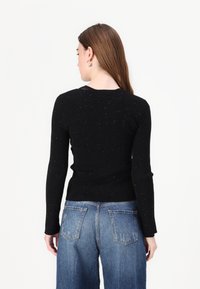 Maglione nero a coste con maniche lunghe, caratterizzato da sottili dettagli luccicanti. Indossato con jeans in denim larghi, mostrando una silhouette aderente.