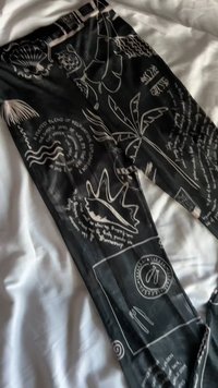 Black leggings featuring white line drawings of shells, plants, and text patterns. The fabric appears smooth with a stretchable design.