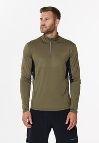 Olivenfarbene, langärmelige Sportoberteil mit einem Viertelreißverschluss, schwarzen Seitenpanelen und weichem, feuchtigkeitsableitendem Material. Minimale Markenkennzeichnung auf der Brust.