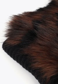 Brun och svart faux päls tyg med en mjuk textur, lager ovanpå ett svart material; har en ludden, voluminös utseende.