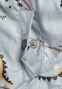 Ljusblått tyg med fantasifulla mönster. Silverfärgad tryckknapp och texturerade detaljer vid kanterna. Slätt, lätt material.