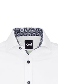 Camicia bianca con colletto interno a fantasia navy e bottoni scuri, realizzata in tessuto morbido con una sottile texture.