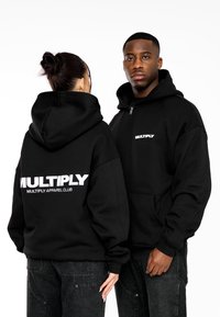 Černé zipové mikiny s kapucí vyrobené z měkké tkaniny, s velkým bílým logem "MULTIPLY" na zadní a přední straně, s běžným střihem a klokaními kapsami.